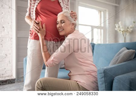 Comfortable Sofa. Mother Of Young Expecting Woman Touching Belly While Sitting On Comfortable Sofa