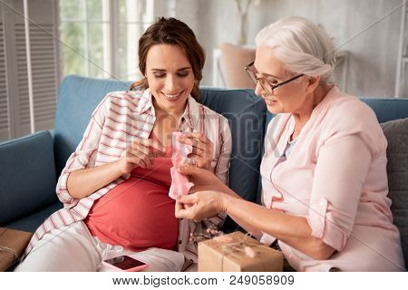 Baby Socks. Aged Grey-haired Woman Wearing Nice Black Glasses Looking At Little Baby Socks