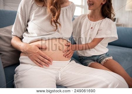 Hand On Belly. Beaming Little Girl Feeling Unforgettable While Putting Her Hand On Pregnant Belly Of