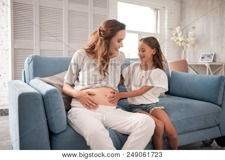 Older Daughter. Appealing Pregnant Mother Feeling Unbelievably Happy Sitting Near Her Older Daughter