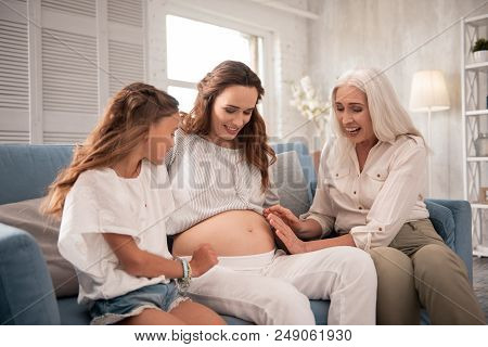 Taking Care. Good-looking Stylish Grandmother And Daughter Taking Care Of Pregnant Woman Sitting Bet