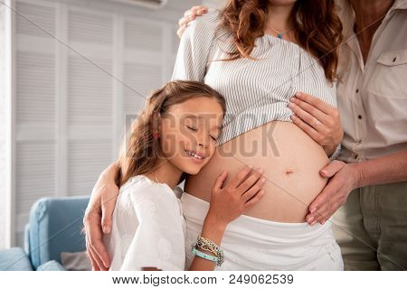 Ear On Tummy. Little Cute Girl With Dark Wavy Hair Putting Her Ear On Pregnant Tummy