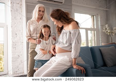 Sofa At Home. Beautiful Pregnant Woman With Long Wavy Hair Sitting On Sofa At Home Surrounding By He