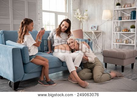 Nice Photo. Cute Modern Girl Making Memorable Photo Of Her Pregnant Mom With Grandmother
