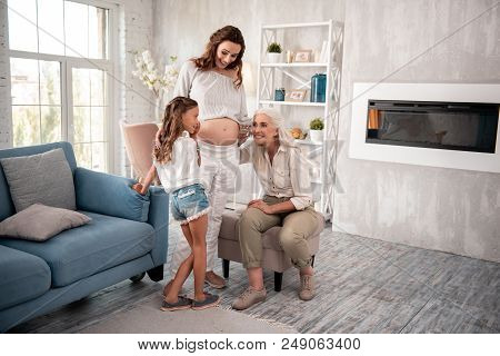 Modern Grandmother. Modern Blonde-haired Grandmother Sitting On Little Armchair Near Pregnant Daught
