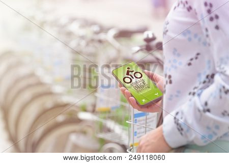 Woman using smartphone to rent bicycle from urban bicycle sharing station
