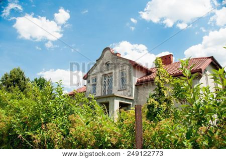 Old House Overgrown With Plants On The Background Of A Blue Sky