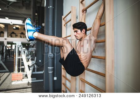 Young Handsome Fit Man In Gym Working Out On Wall Bars, Holding L-sit.