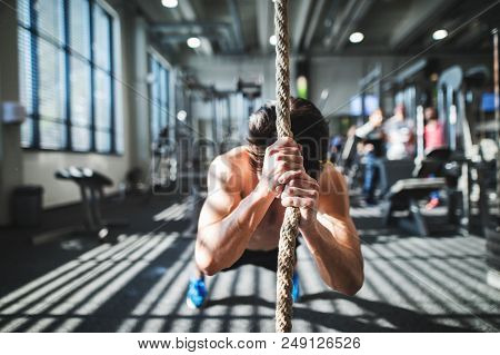 Young Fit Man Working Out In Gym. A Boy In A Plank Holding Onto A Climbing Rope.
