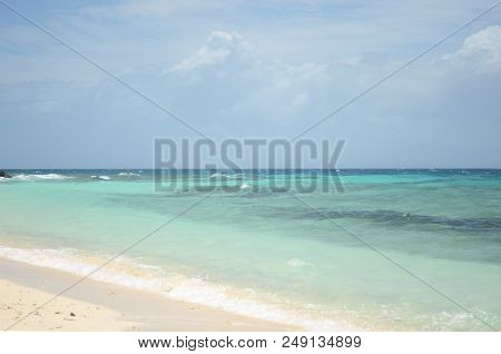 The Waters Of A Tropical Beach Range From Aqua To Dark Blue. The Sand Is Pale Gold. Storm Clouds Are