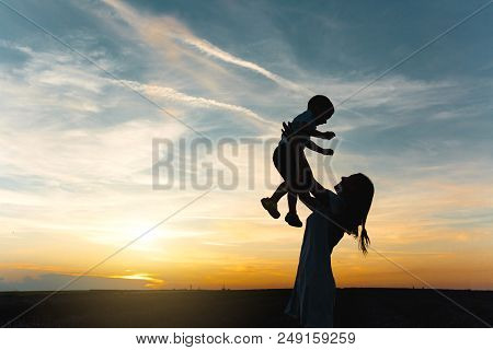 Silhouette Of Young Woman High Toss Up Little Cute Child Baby Boy On Nature, Sunset Horizon Backgrou