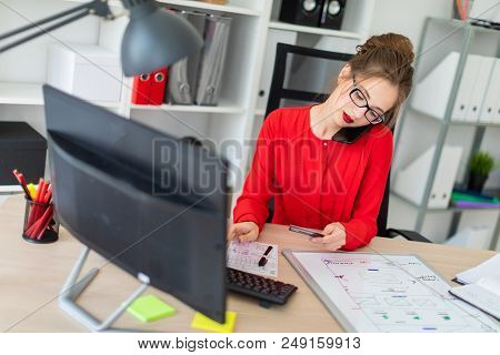 Beautiful Young Girl In Glasses And A Red Shirt Is Working In The Office. Photo With Depth Of Field.