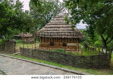 A Rural House Under A Thatched Roof With Small Windows In The Wall Behind A Wattle Fence In A Pictur