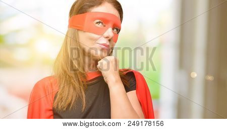 Middle age super hero woman wearing red mask and cape thinking and looking up expressing doubt and wonder