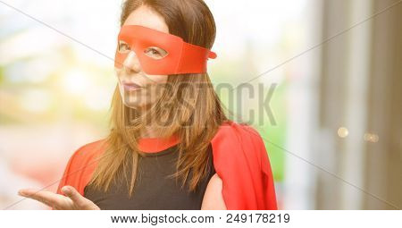 Middle age super hero woman wearing red mask and cape holding something in empty hand