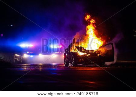 Car On Fire At Night With Police Lights In Background