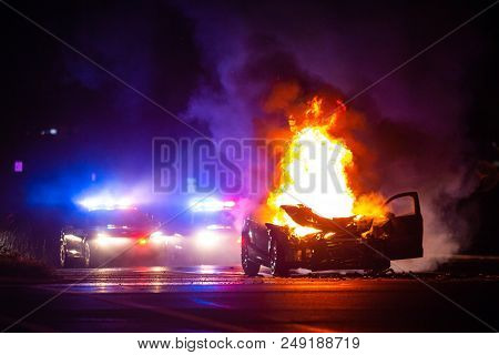 Car On Fire At Night With Police Lights In Background