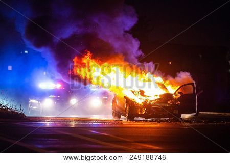 Car On Fire At Night With Police Lights In Background
