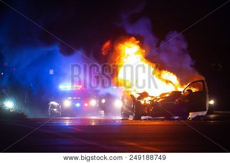 Car On Fire At Night With Police Lights In Background
