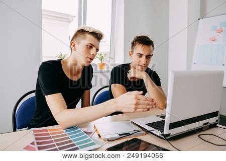Graphic Designers Working With Laptop And Color Samples. Two Confident Young Men Looking At Laptop M