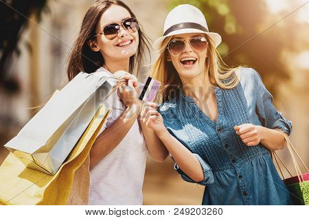 Girls In Sunglasses With Credit Card In Their Hand Laughing Into Camera. Reducing Stress By Buying. 
