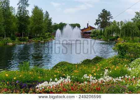 A Magnificent Variety Of Flowers Growing On The Shore Of A Pond With Fountains