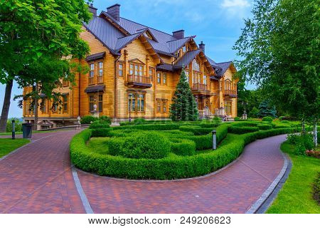 A Ramshackle Cobbled Pathway In A Well-kept Park In Front Of A Huge Wooden Mansion Among Tall Green 