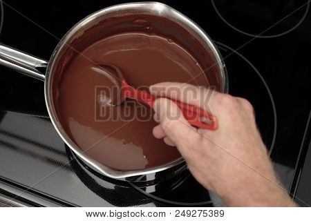 100% Cocoa And Water Being Stirred With A Red Spoon In A Pan By A Hand Of An Adult Male Closeup. Han