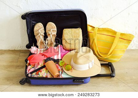 Open Suitcase Fully Packed With Folded Women's Clothing And Accessories On The Floor. Woman Packing 