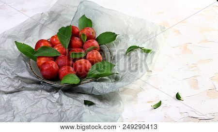 Bunch Of Red Sweet Plums With Green Leaves On A Light Background. Top View, Space For Text.