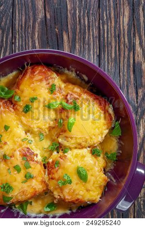 Cheesy Smothered Pork Chops Sprinkled With Basil Leaves In A Baking Dish On An Old Dark Rustic Table