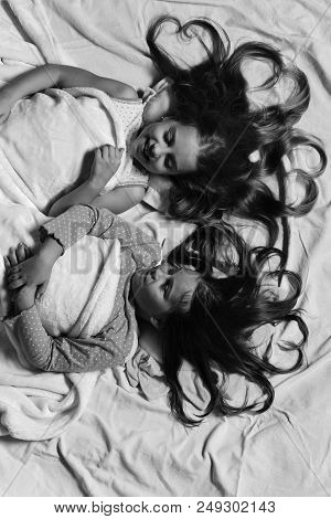 Pajama Party Concept. Girls Lie On Pink Bed Sheets Looking At Each Other. Kids With Smiling Faces An