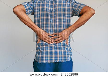 Close-up View Of A Young Man With Pain In Kidneys On Gray Background. Young Man With Back Ache Clasp