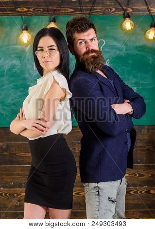 Man With Beard And Teacher In Eyeglasses Stand Back To Back, Chalkboard On Background. School Staff 