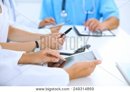Doctor Using Tablet Computer At Medical Meeting, Closeup. Group Of Colleagues At The Background.