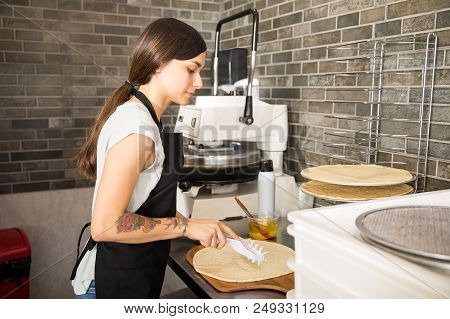 Young Chef Wearing Black Apron Uniform Preparing Pizza Bread With Raw Dough Using Dough Punch Roller