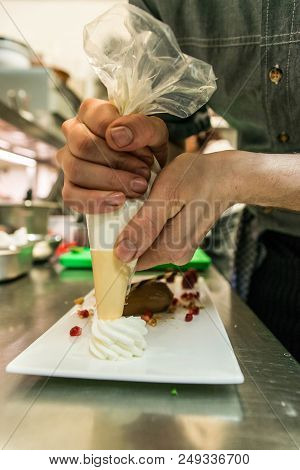 Cook Adding Cream To A Piece Of Brown Mousse Au Chocolate Sweet Dessert And Decoration On A White Pl