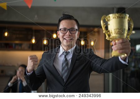 Asian Businessman Raising Up Hand And Holding A Golden Trophy Cup To Cheerful And Celebrated His Suc