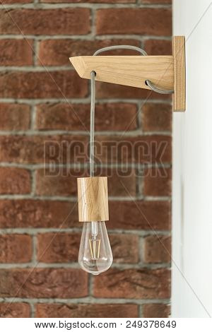 Hanging, Wooden Light Shade Lamp With Bulb. Lighting Bulb Against A Brick Wall Background.