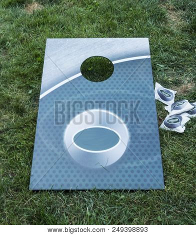 A Aqua Colored Corn Hole Game Is On The Grass With White Bean Bags On The Side.