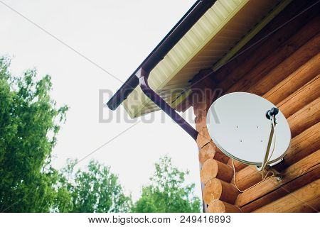 Satellite Dish On The Wall Of The House. Antenna Is White. The House Is Made Of A Wooden Beam Of Bro