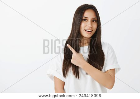 Intrigued Happy Young Woman With Tanned Skin And Dark Hair, Pointing At Upper Left Corner And Talkin