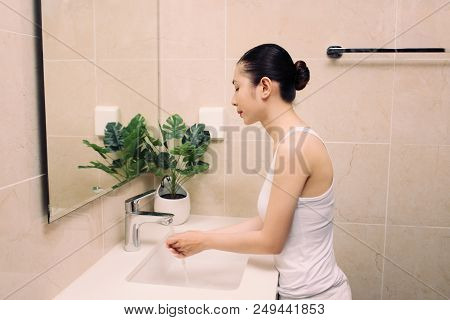Woman Washing Her Face With Water Above Bathroom Sink.