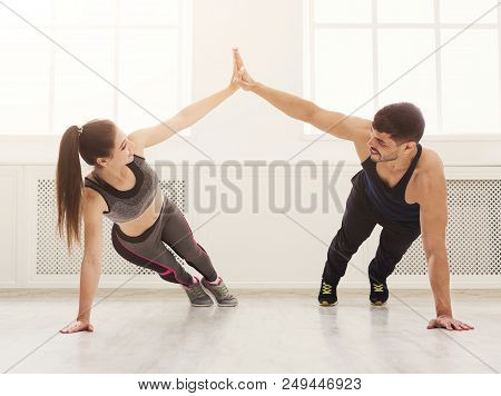 Happy Sporty Couple Giving High Five To Each Other While Doing Push Up Together In Gym. Unity And Su
