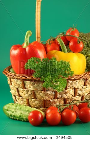 Brokolice, paprika, okurky a rajčata v košíku na zeleném pozadí.