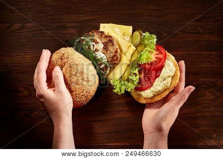 Woman's Hands Holding Traditional American Burger On Wooden Background, Top View, Close-up.