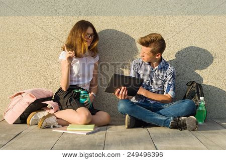 School Children Teens Sit On The Gray Wall, Read Textbooks, Drink Water, Look At The Tablet.the Girl