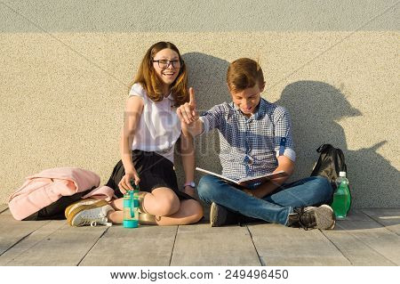 Happy Students On Campus Pathway, Teenagers Sit On The Gray Wall, Read Textbooks, Drink Water, Look 