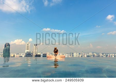 Rear View Of Female Tourist In Infinity Pool Of Marina Bay Singapore Skypark Looking At City In Sing