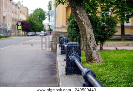 Black, Forged, Metal Railing On A Low Sandstone Wall Recede Into The Distance. Grass And Trees Can B